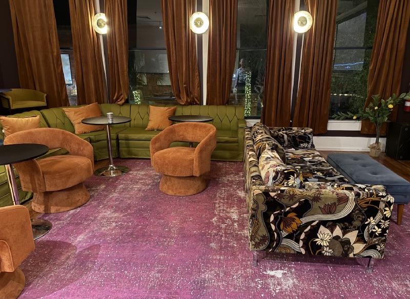 Very hip lounge furniture in burnt orange and olive green with a retro mid century couch with paisley type pattern in the same green and orange colors. A lounge room at the Tigre Island Room in Fernandina Beach, FL