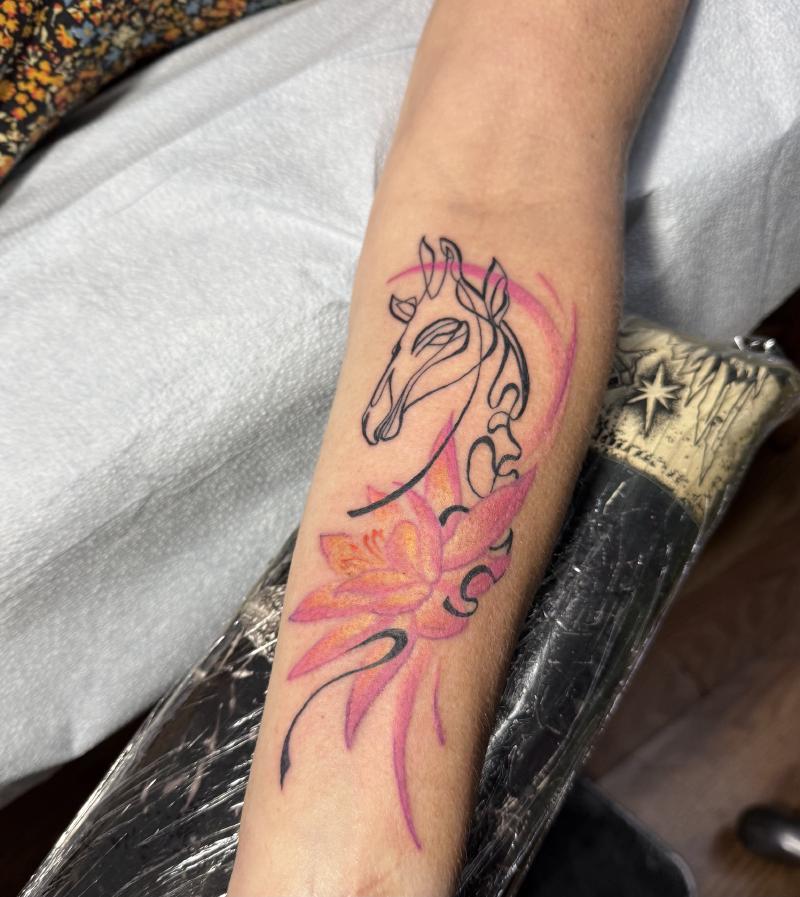 A new tattoo I got in 2026 on my right forearm that is a slanted pink lotus that is whooshing into a giraffe that’s drawn in a one-line ribbon style
